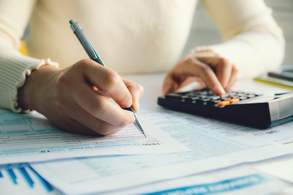 A person filling out tax forms with a pen and using a calculator.